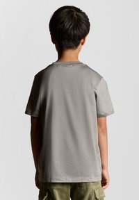 Grå bomulds t-shirt med korte ærmer, rund halsudskæring og en glat tekstur, set fra ryggen. Båret med olivengrønne cargo shorts.