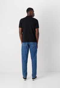 Schwarzes Polohemd, kurze Ärmel, lässige Passform; kombiniert mit lockeren hellblauen Jeans und schwarzen Sneakers. Rückansicht gezeigt.