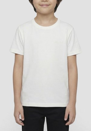Enfant portant un t-shirt blanc uni à manches courtes et un pantalon noir, debout devant un fond blanc.