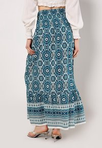 Maxikjol i blått och vitt med blommönster och geometriska mönster, resår i midjan och flerradig design, tillverkad av lätt tyg.