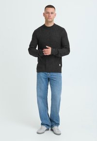 Mørkegrå ribbet striktrøje med rund halsudskæring, parret med lys blå lige ben jeans og grå sneakers. Simpelt design og tekstur.