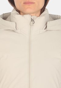 Giacca zip-up beige chiaro con colletto alto. Realizzata in materiale liscio e leggero; presenta una zip frontale e dettagli di cucitura minimi.