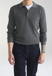 Polo grigio a maniche lunghe con tessuto lavorato, caratterizzato da un colletto e tre bottoni, abbinato a jeans blu scuro.