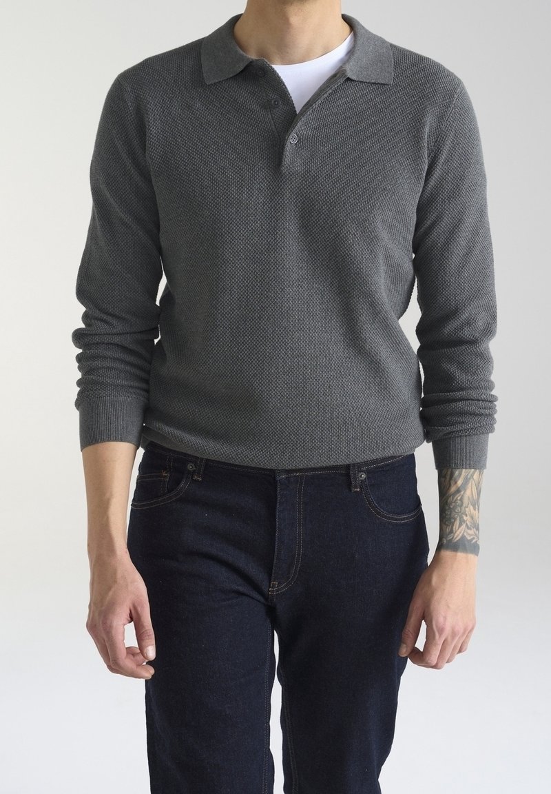 Polo grigio a maniche lunghe con tessuto lavorato, caratterizzato da un colletto e tre bottoni, abbinato a jeans blu scuro.