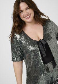 Svart paljett-topp med V-ringning och korta ärmar, med en sidenband-detajl fram. Tyget har en glänsande, reflekterande yta.