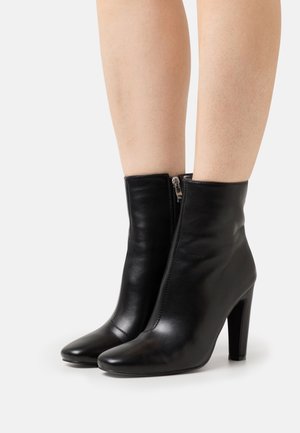 Bottines en cuir noir au design épuré, à bouts pointus et avec une fermeture éclair latérale. Elles sont dotées d'un talon haut et d'une texture lisse.