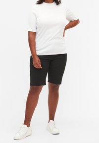 Top blanco de manga corta con textura acanalada, combinado con pantalones cortos negros hasta la rodilla y zapatillas blancas, creando un conjunto casual y cómodo.