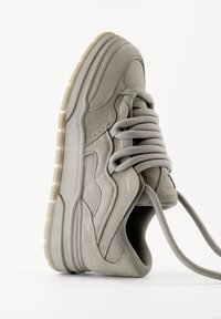 Grå mockaskor med en tjock gummisula, runda snören och strömlinjeformat design. Har texturerade paneler och subtila sömdetaljer.