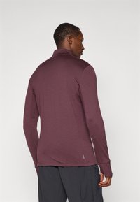 Pulover cu mâneci lungi, de culoare burgundă, cu guler, realizat dintr-un material ușor, având cusături plate și un mic detaliu logo pe lateral.