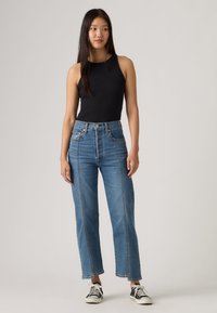 Μαύρο αμάνικο τοπ με ριγέ υφή, συνδυασμένο με μπλε τζιν ψηλόμεσο παντελόνι σε ίσια γραμμή και δύο έντονες κάθετες ραφές. Μαύρα αθλητικά παπούτσια.