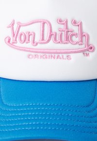 Casquette blanche avec une visière bleue, comportant le texte brodé en rose "Von Dutch Originals" sur le devant. Tissu lisse avec des détails de coutures visibles.