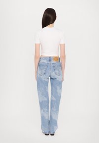 Light blue denim jeans with a loose fit, featuring a faded floral pattern, five pockets, and a tan leather brand tag on the waistband.