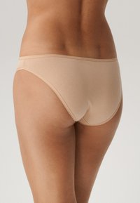 Beżowa bawełniana bielizna hipsterska o gładkiej fakturze, niskim stanie i subtelnym przeszyciu, bez widocznych elementów metalowych lub wzorów.