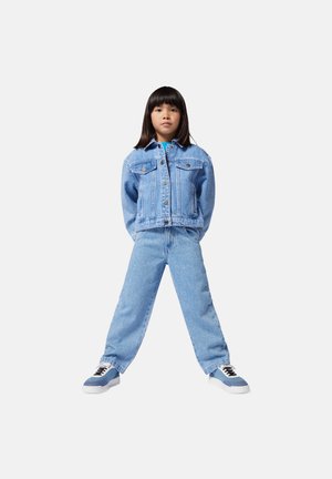 Giacca di jeans azzurro chiaro con tasche frontali e chiusura a bottoni, abbinata a jeans a vestibilità ampia dello stesso colore. Sneakers bianche e blu completano l'outfit.