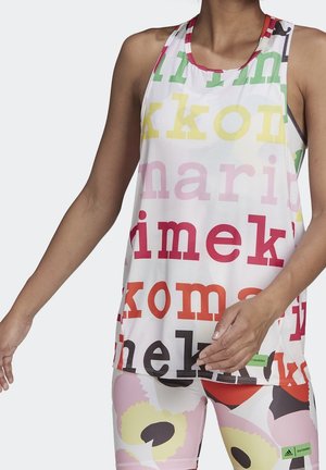 Vrouw die een witte mouwloze top en bijpassende legging draagt met kleurrijke grote tekst en abstracte bloemenprint, staand met ontspannen armen.