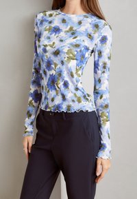 Długi rękaw ribbed top w jasnoniebieskim kolorze z zielonym i niebieskim floralnym wzorem. Falbaniasty dół, dopasowany krój, zestawiony z ciemnymi spodniami.