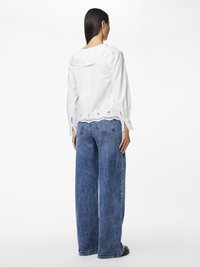 Bluză albă din bumbac cu guler fluturat și detalii din dantelă cu găurele la tiv, asortată cu blugi blue denim cu picioare largi.
