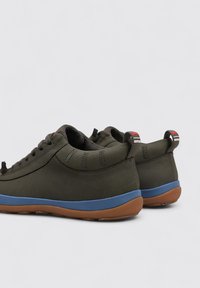 Sneaker verde scuro con tomaia liscia, forma arrotondata, suola intermedia blu e suola esterna in gomma bruna texturizzata. I dettagli includono il logo sul retro.