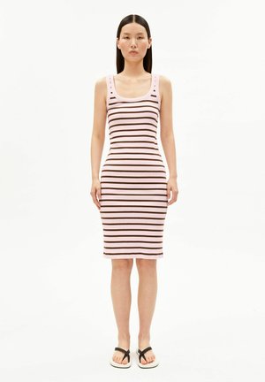 Vrouw staat frontaal, draagt een roze mouwloze knielange jurk met horizontale bruine strepen en zwarte teenslippers.