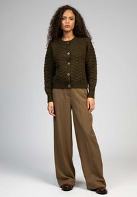 Cardigan en tricot vert olive avec une texture ondulée, fermeture à boutons et ourlet côtelé ; associé à un pantalon large marron à taille haute.