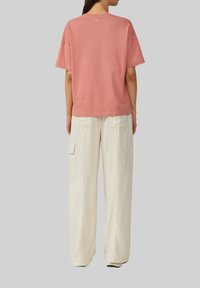 Różowa koszulka z bawełny o luźnym kroju i krótkich rękawach, zestawiona z jasnymi, kremowymi spodniami o luźnym kroju z bocznymi kieszeniami.