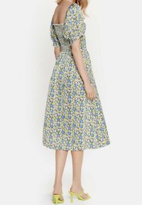 Midi dress dengan corak bunga, lengan menggelembung, bodice yang pas, dan rok melebar. Warna termasuk biru, kuning, dan putih. Dipadukan dengan sepatu hak tinggi hijau.