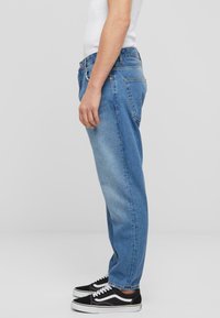 Jeans de mezclilla azul claro con corte recto, que cuentan con una cintura alta, diseño de cinco bolsillos y un ligero desgaste, combinados con zapatillas negras.