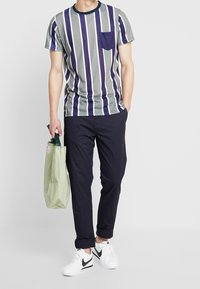 Stribet t-shirt med rund hals, korte ærmer, grå og lilla farver, med en brystlomme. Sammen med navy bukser og hvide Nike sneakers.