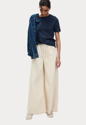 T-shirt en coton marine associé à un pantalon large beige et une veste en denim portée décontractée sur l'épaule. Tissu doux et coupe décontractée.