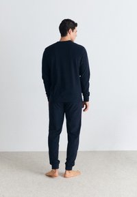 Souprava z námořnického modrého bavlněného materiálu obsahující mikinu a kalhoty, s žebrovanými manžetami a lemem. Jednoduchý design, měkká textilie a volný střih pro pohodlí.