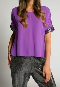 Lila kortärmad topp i lätt material, med glittrande svarta paljetter på ärmarna. Buren med blanka svarta paljettbyxor.