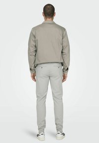 Camisa de color gris claro con cuello, pantalones ajustados de color gris claro y zapatillas blancas con detalles negros. Tejido suave y detalles mínimos.