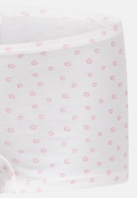 Tissu blanc avec un motif de petits pois roses, montrant un gros plan de la taille et de la couture d'un vêtement.