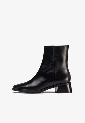 Bottine en cuir noir avec un bout pointu et un talon bloc de hauteur intermédiaire. Présente une texture lisse et des détails de couture minimes sur les côtés.