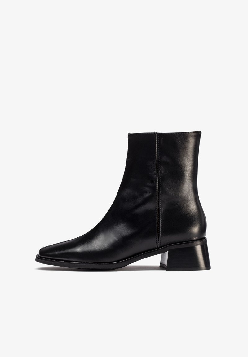 Botín de cuero negro hasta el tobillo con puntera afilada y tacón bloque de altura media. Presenta una textura suave y detalles de costura mínimos en los laterales.