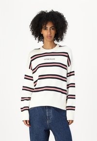 Valge särk roosa ja musta horisontaalsete triipudega. Omab ümarat kaelust ja soonikuid varrukates; "GUESS JEANS" logo on keskendatud rinnal.