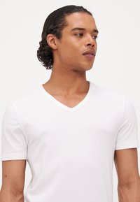 Weißes V-Ausschnitt-T-Shirt aus weichem Baumwollstoff, mit kurzen Ärmeln und glatter Textur. Einfaches und klassisches Design ohne Muster.