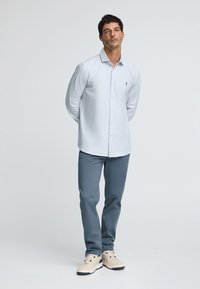 Camicia button-up azzurra chiara con motivo a quadretti, abbinata a pantaloni grigi chiari e sneakers beige. Design casual, aderente.