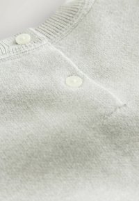 Hele halli kudumüts, millel on sooniline kaelus ja kaks valget nööd lahtise külje peal. Pehme tekstuur sujuva viimistlusega.