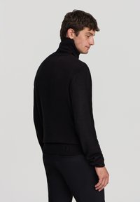 Maglione collo alto nero con colletto e polsini a costine, realizzato in un morbido tessuto a maglia. Design aderente con una texture liscia e colore uniforme.