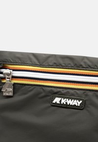 Primo piano di una pochette nera K-Way con una cerniera a strisce multicolori e un tirazip in metallo con il logo K-Way.