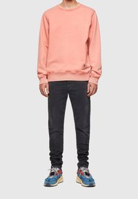 Light pink sweatshirt with crew neckline, ribbed cuffs, and hem, paired with dark grey jeans and multi-colored athletic sneakers.