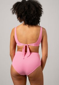 Rosa bikinitop med knytning bak, breda axelremmar och högmidjade underdelar. Materialet verkar vara texturerat med en slät yta.