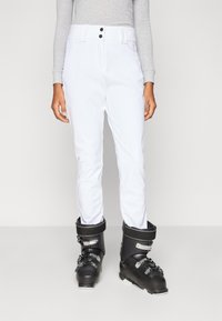 Λευκό σκι παντελόνι με κομψό σχεδιασμό και δύο μαύρα κουμπιά στη μέση, συνδυασμένο με μαύρα παπούτσια σκι με ασημένιες λεπτομέρειες.