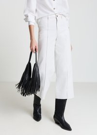 Weiße Hosen mit weitem Bein und sichtbaren Nähten, kombiniert mit einer schwarzen Handtasche mit Fransen und schwarzen Western-Stiefeletten. Saubere, moderne Ästhetik.