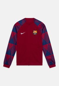 Nike track jakke i rød med blå geometriske mønstre på ærmerne, med en forreste lynlås og et broderet FC Barcelona-logo.