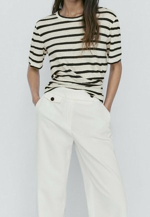 Cream striped t-shirt with black stripes, short sleeves, paired with high-waisted white wide-leg trousers featuring a side button detail.