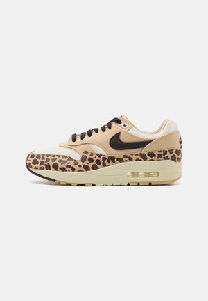 Beige sneaker met zwarte accenten, luipaardprint op de neuzenkap en stevige crèmekleurige zool met zichtbare luchtunit. Heeft getextureerde materialen en veters.