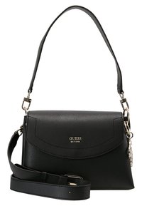 Mustakasta nahkaolkalaukkua, jossa on käännettävä läppä, kultaiset yksityiskohdat ja säädettävä hihna. Etupuolella logo "GUESS EST 1981".