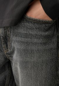 Jeans din denim negru cu un finisaj texturat, având cusături vizibile și un buzunar frontal. Purtați cu o cămașă închisă la culoare la talie.